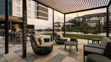 An outdoor seating area with tables and chairs, a pergola, and a view of the surrounding buildings.