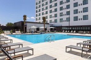 A hotel pool area with lounge chairs, a swimming pool, and a modern building in the background. - Even Hotel Orlando Universal Blvd By Ihg (Orlando)