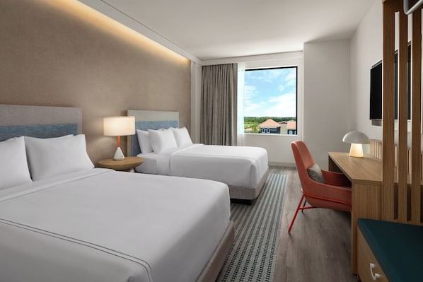 A hotel room with two beds, a desk, a chair, a TV, and a window with a view of buildings. - Even Hotel Orlando Universal Blvd By Ihg (Orlando)