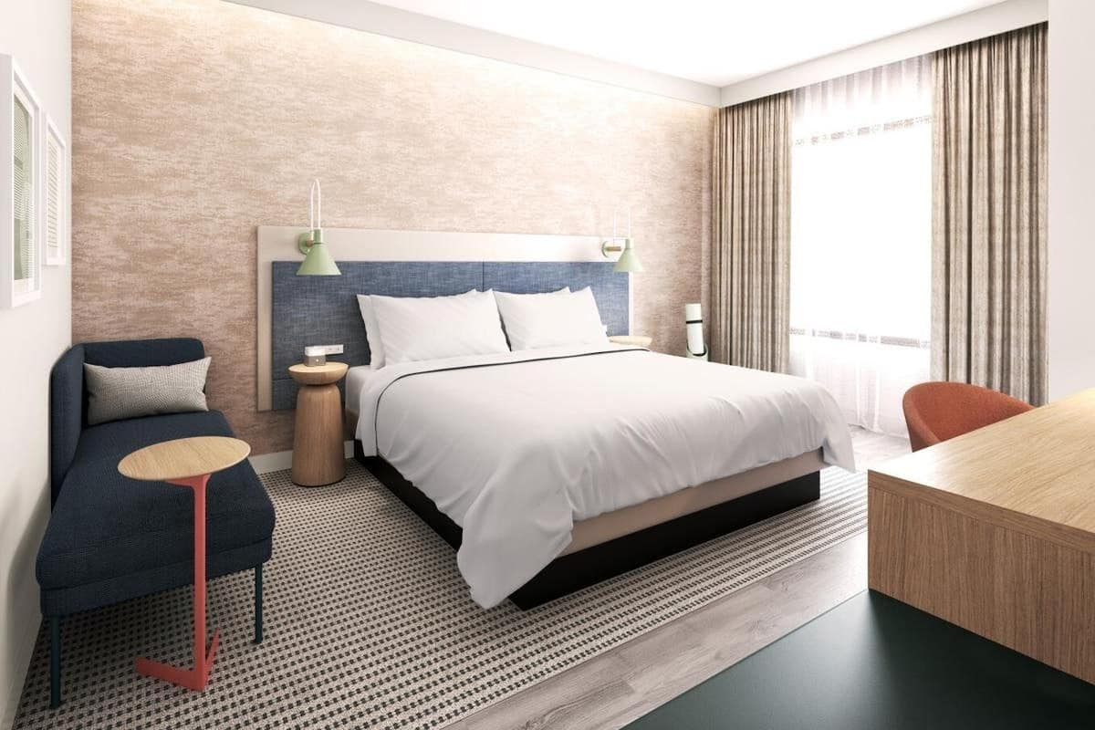 A modern hotel room with a large bed, a desk, a sofa, and two side tables.