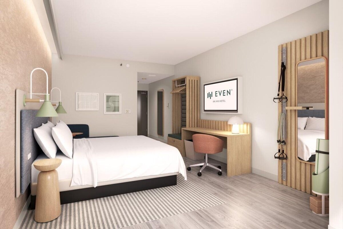 A modern hotel room with a large bed, a desk, a wardrobe, and a mirror.