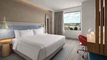 Una habitación de hotel moderna con una cama grande, lámparas de noche, un escritorio con silla y vistas a edificios a través del ventanal.