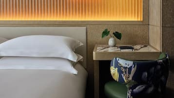 Une chambre d’hôtel avec un lit, une table de chevet, un vase avec une plante et une chaise au motif coloré.