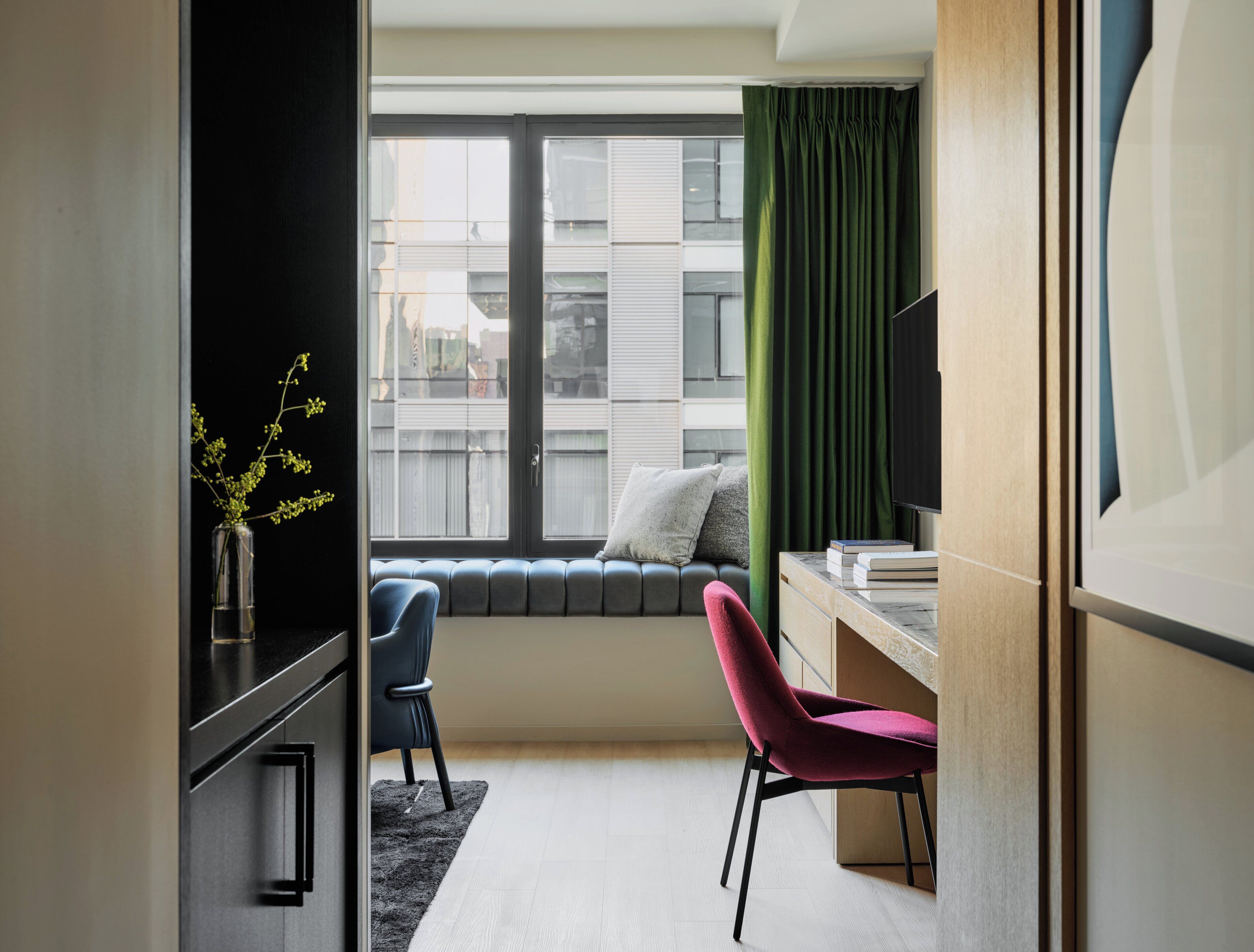 Een moderne kamer met raam, bureau, stoel en een kleine plant.