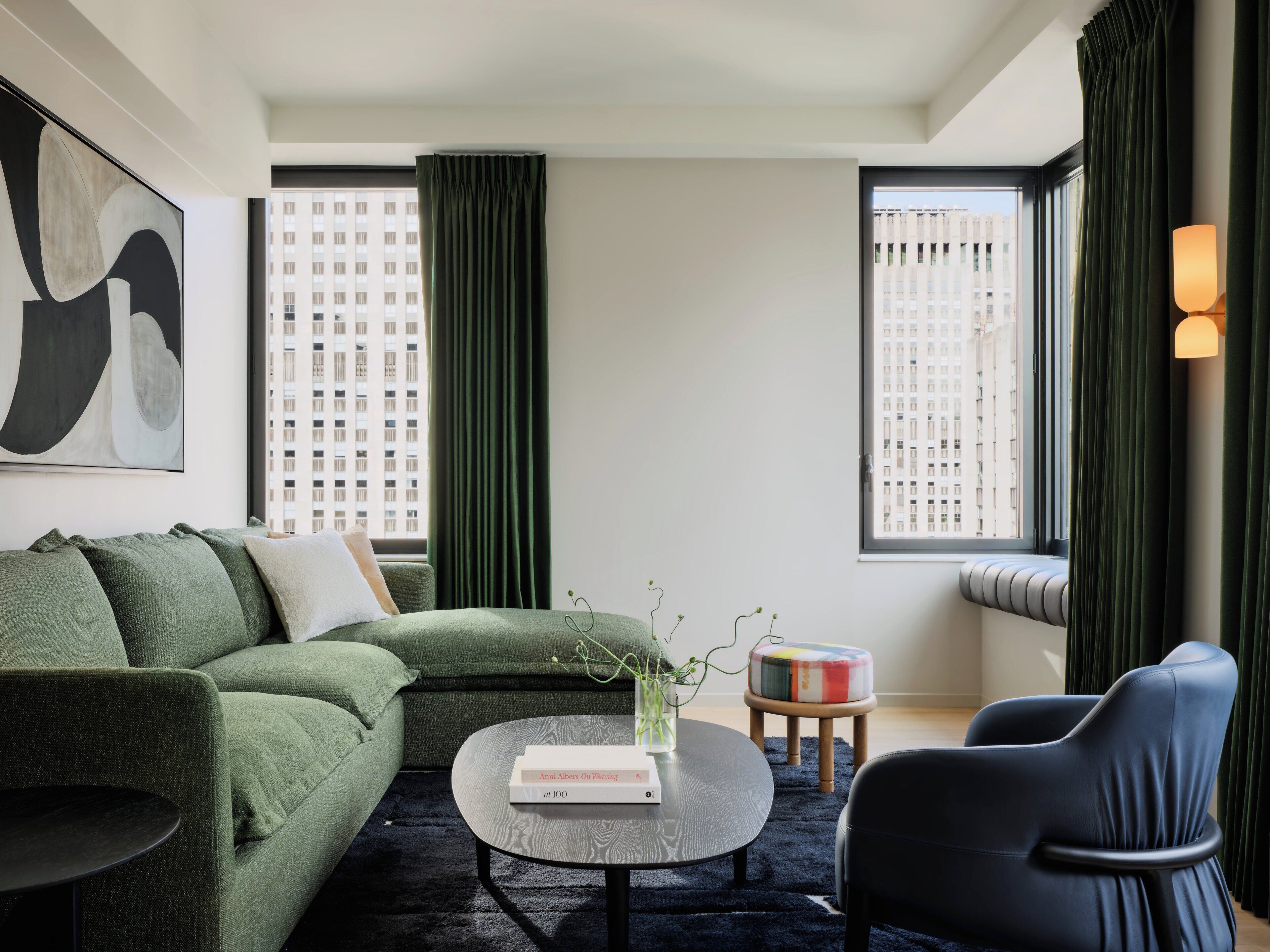 A modern living room with a sectional sofa, a round coffee table with a book, a small stool, and a black chair.