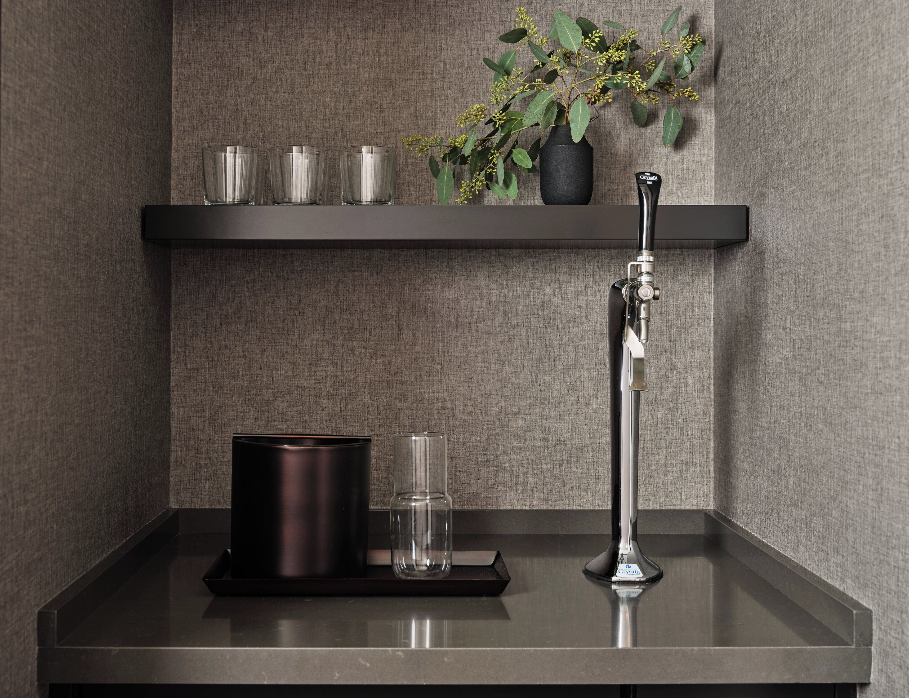 Une salle de bain avec un comptoir noir, un vase noir orné de feuilles vertes et un robinet chromé haut.