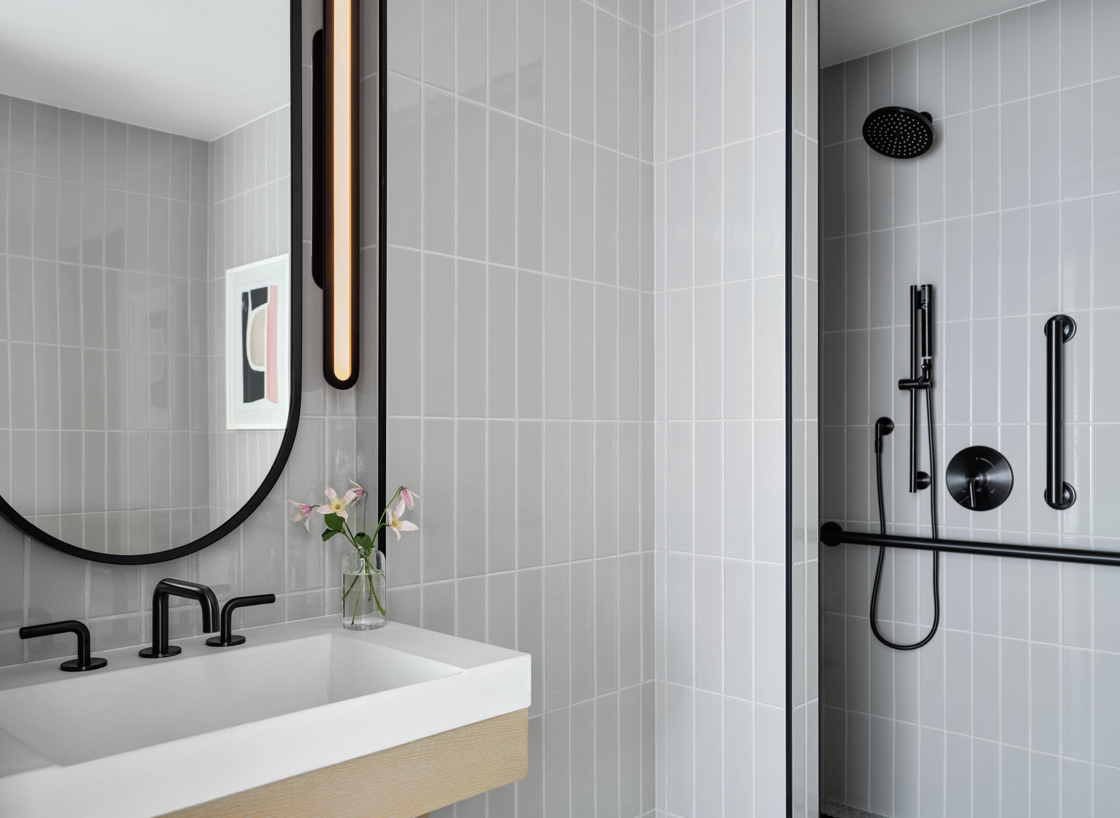 A modern bathroom with a white sink, black fixtures, a glass shower enclosure, and a framed picture on the wall.