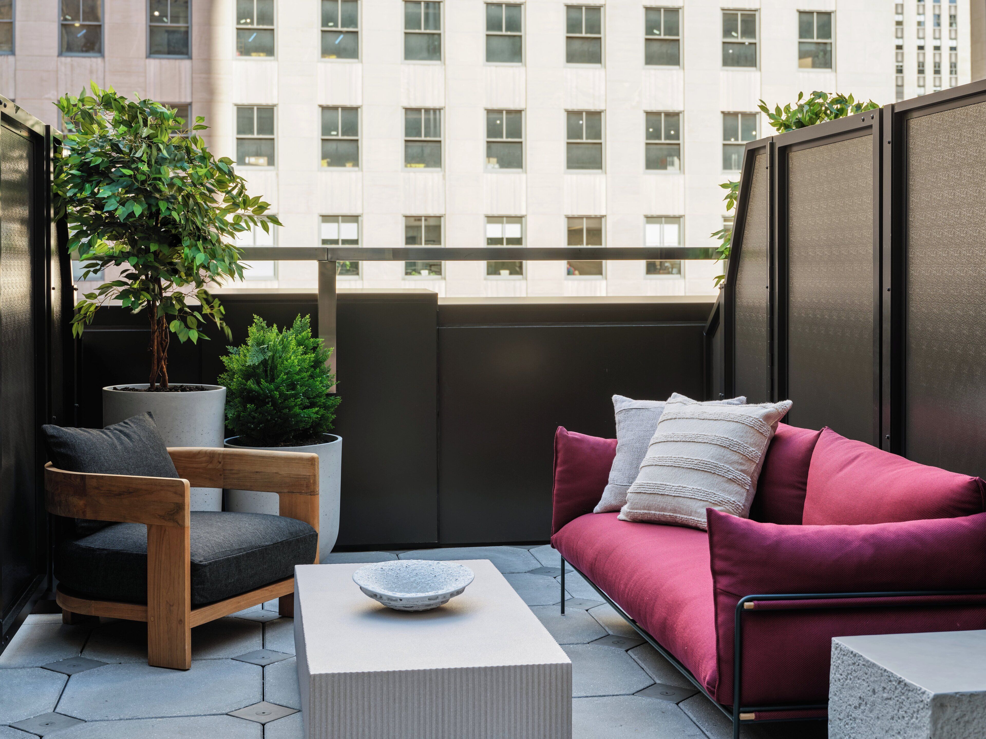 A balcony with a wooden chair, a red sofa, a small table, and potted plants.