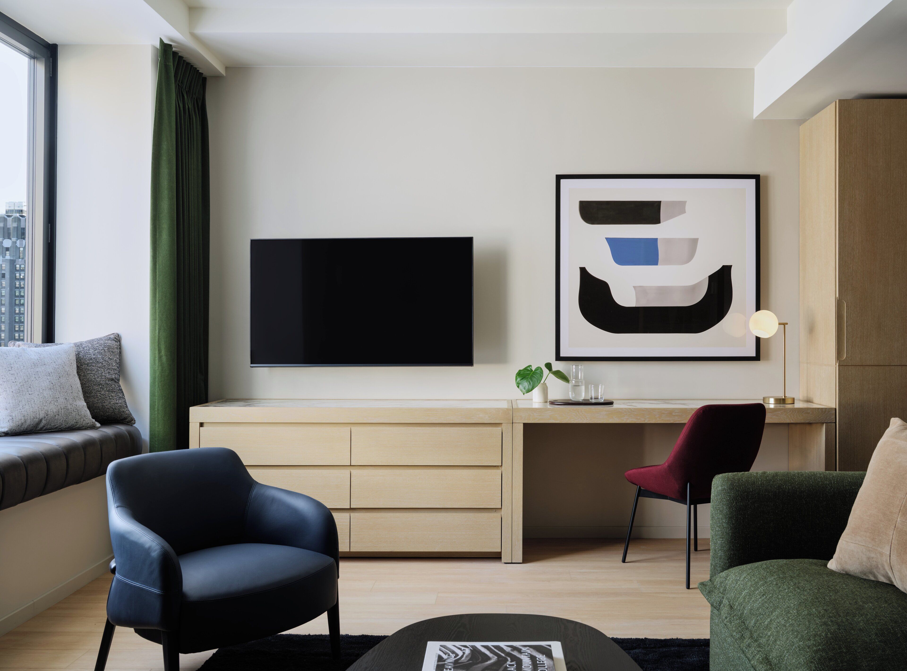 Un salon moderne doté d’un téléviseur à écran plat, d’un bureau, de deux fauteuils, d’une table basse et d’une œuvre d’art abstraite encadrée.