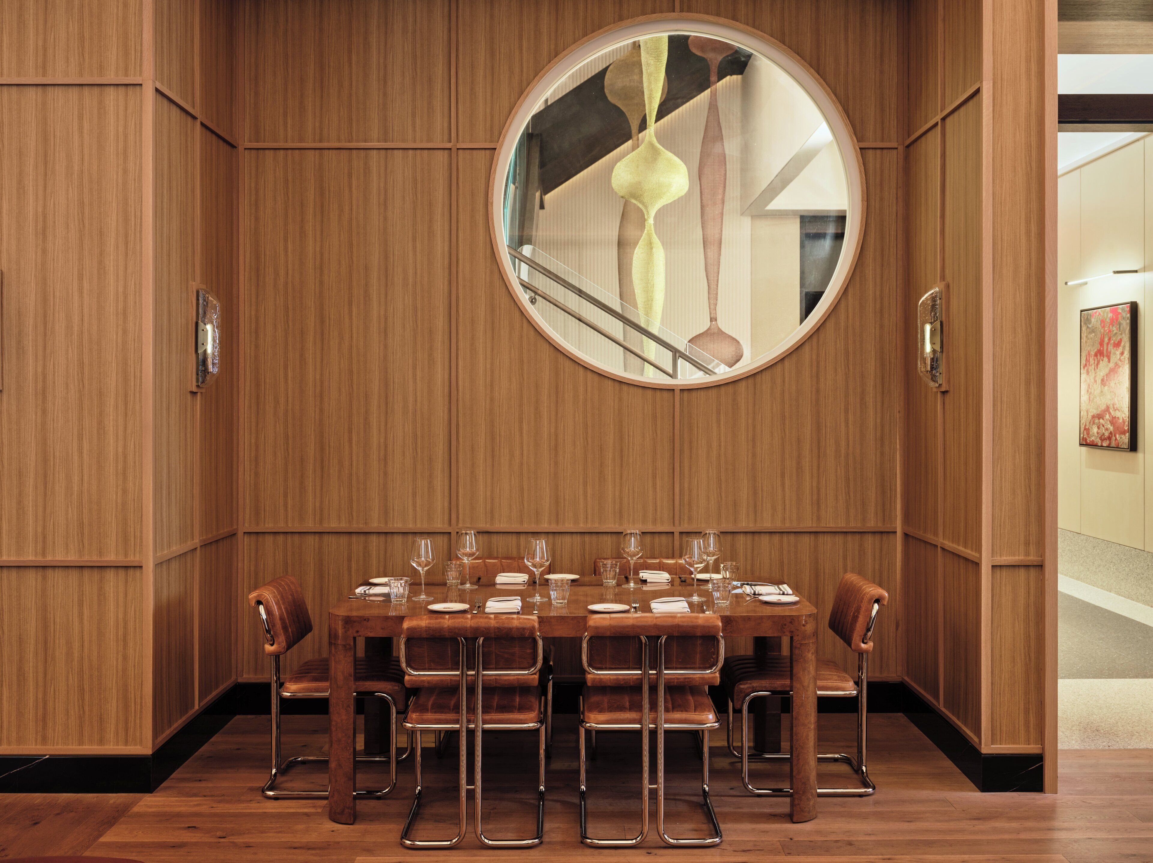 A dining area with a round mirror, wooden paneling, and a table set for six with chairs.