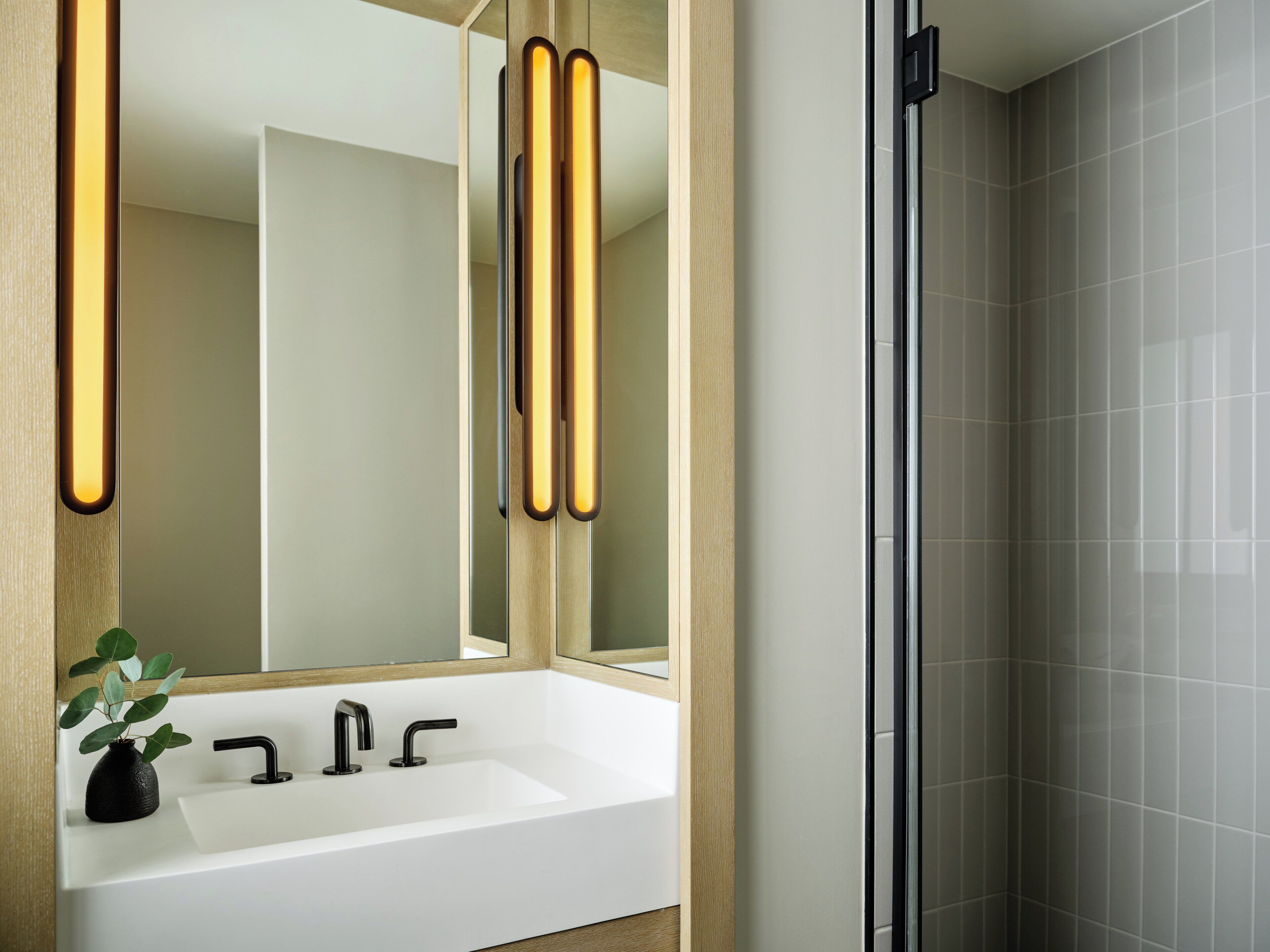 A bathroom with a white sink, black faucet, and a mirror with vertical light strips.
