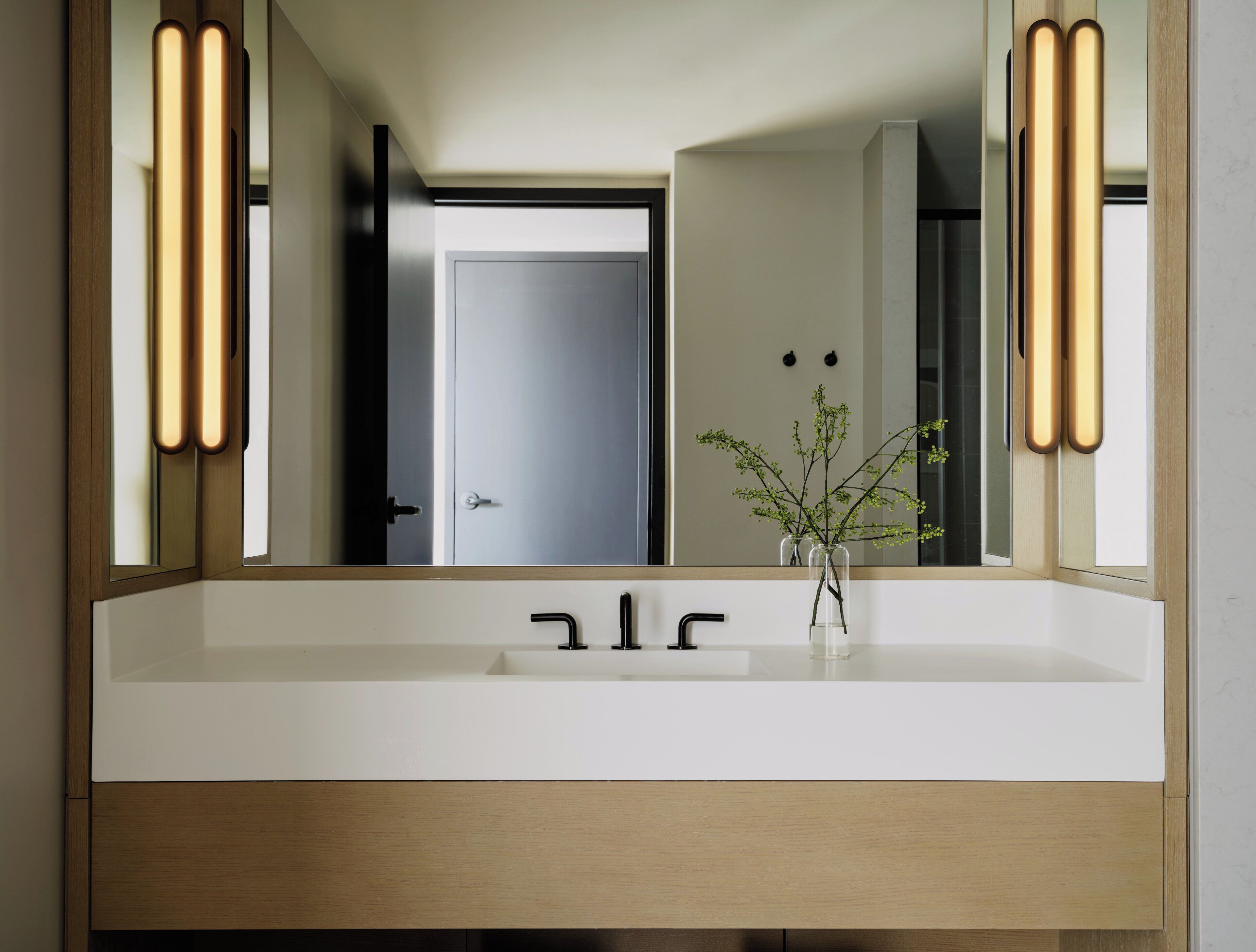 A bathroom with a white sink, a mirror, and a plant in a clear vase.