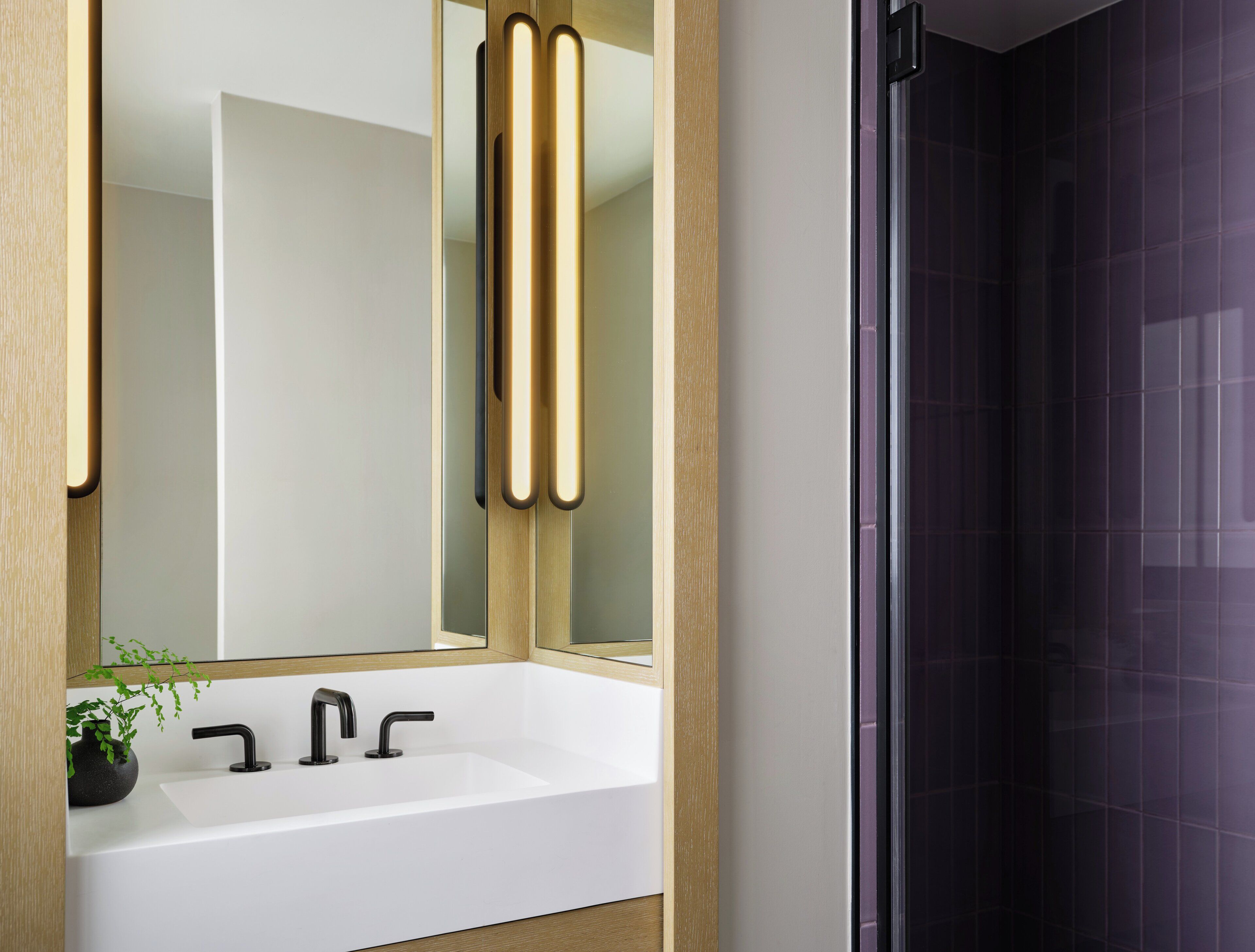 A modern bathroom with a white sink, black faucets, and a mirror with vertical light strips.
