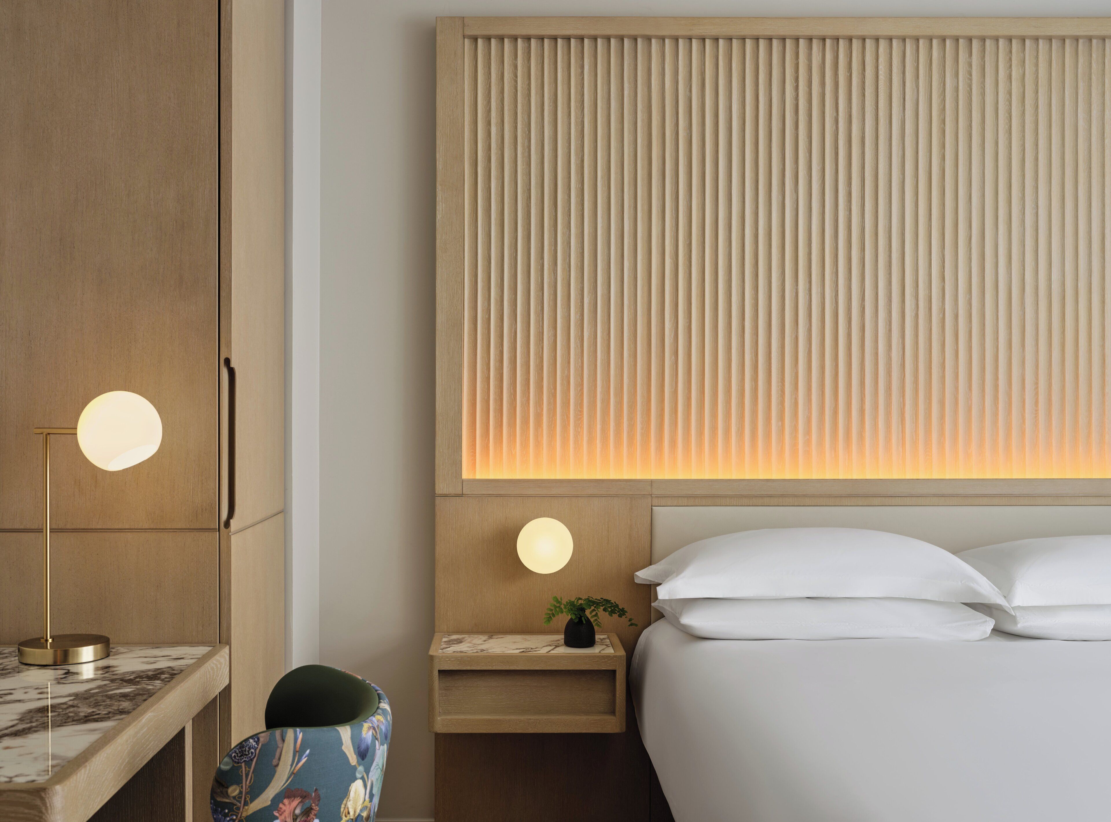 A hotel room with a bed, bedside table, lamp, and a wall with vertical blinds.