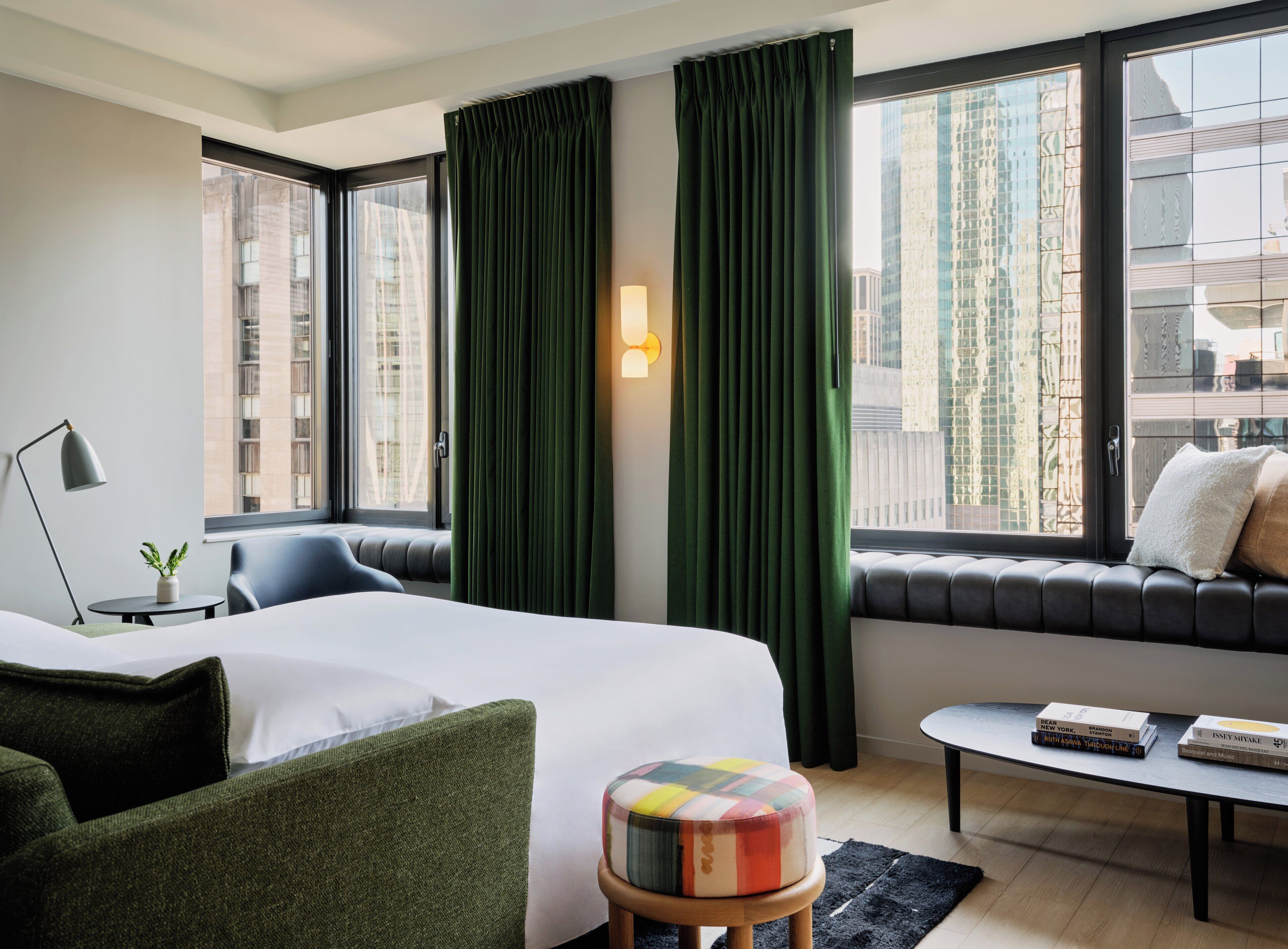 A hotel room with a bed, a sofa, a small table, a lamp, and a window with curtains.
