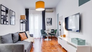 A modern living room with a sofa, a dining table with chairs, a TV mounted on the wall, and a large window with curtains. - BDC - Zenit 1BDR @Vaticano (Rome)