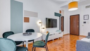 A modern living room with a round dining table, green chairs, a flat-screen TV, a sofa, and a wooden door. - BDC - Zenit 1BDR @Vaticano (Rome)