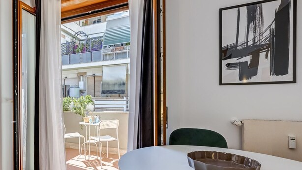 A room with a white table, a green chair, and a view of a balcony with outdoor furniture. - BDC - Zenit 1BDR @Vaticano (Rome)