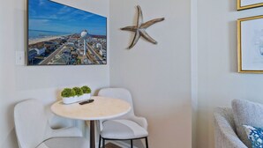Ein Zimmer mit einem runden Tisch, zwei Stühlen, einer Meeressterne-Dekoration, einem gerahmten Bild und einer Pflanze auf dem Tisch.