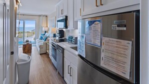 Eine moderne Küche mit einem Edelstahl-Kühlschrank, einer Mikrowelle und einer Kaffeemaschine. Durch die Schiebeglastüren bietet sich Meerblick.