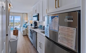 A modern kitchen with a stainless steel refrigerator, a microwave, and a coffee maker. There is a view of the ocean through the sliding glass doors. - 1 Bedroom Oceanfront - Walk right out to the beach! (Ocean Isle Beach)