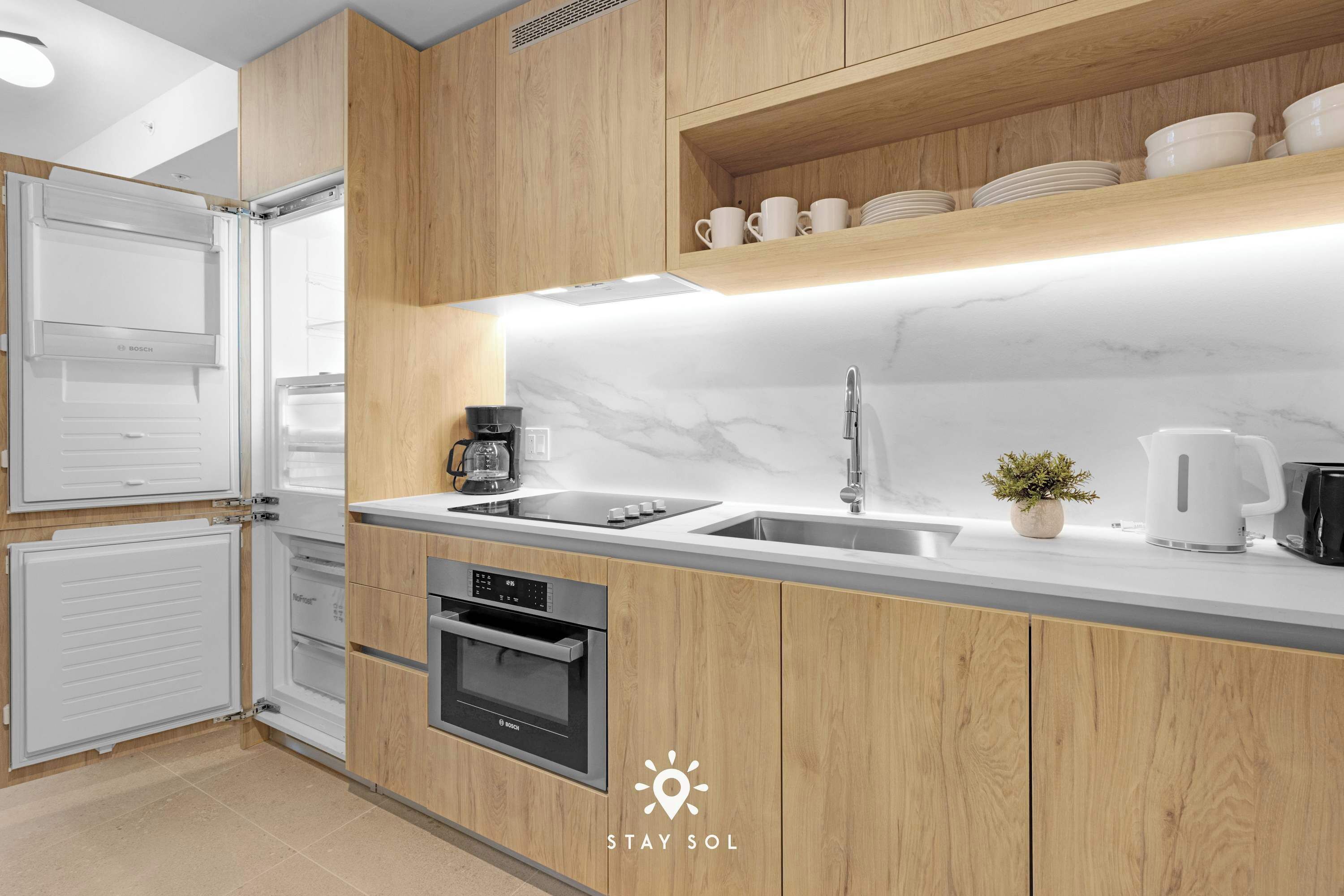 Een moderne keuken met houten kastjes, een inbouwoven, een spoelbak en een koffiezetapparaat.