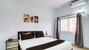 Cama bem arrumada com cabeceira escura, mesa de cabeceira com telefone e ar condicionado fixado na parede.