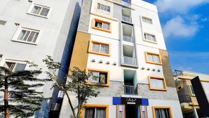 Edifício de vários andares com design arquitetônico moderno, apresentando uma combinação de fachadas brancas e cinzentas, molduras de janelas laranja e uma entrada visível com uma placa.
