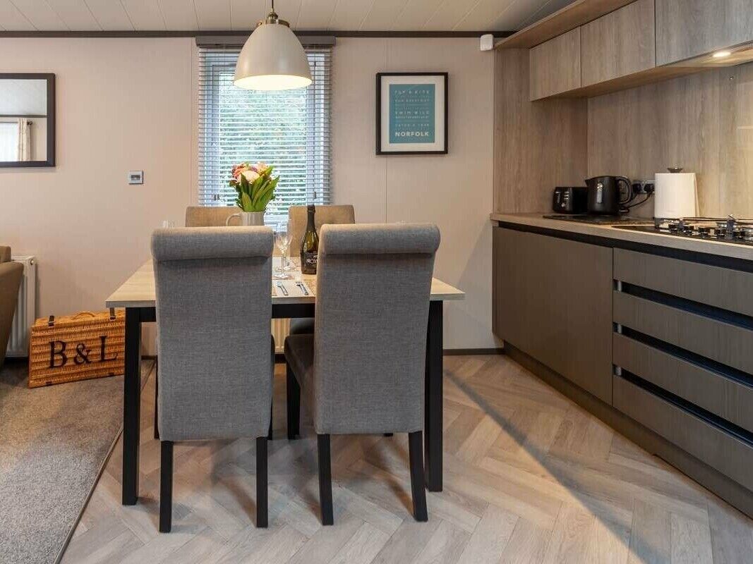 A modern kitchen with wooden cabinets, a dining table with two grey chairs, and a pendant light.