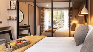 A modern hotel room with a large bed, a desk, and a view through a sliding door to an outdoor area. - Wildwood - Kelling Heath Holiday Park - 16335 (Holt)
