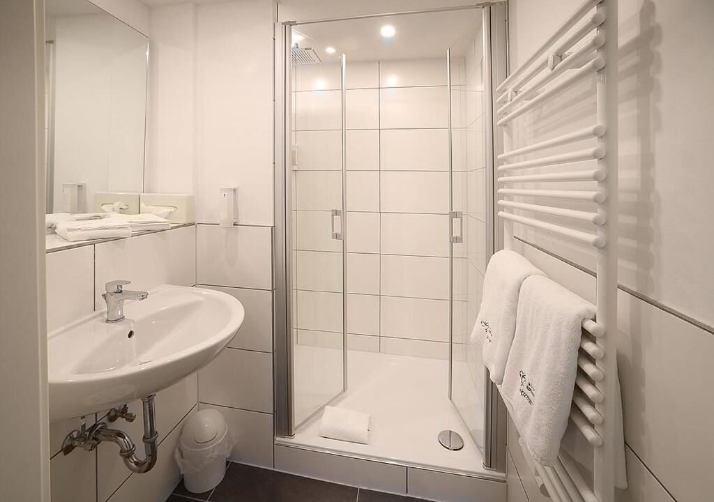 Un baño moderno con cabina de ducha de vidrio, un lavabo blanco con espejo y un perchero para toallas.