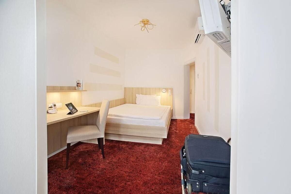 A hotel room with a bed, a desk, a chair, and a suitcase.