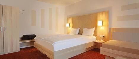 A hotel room with a large bed, bedside tables, a wardrobe, and a small table with magazines.