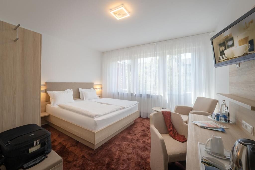 A hotel room with a bed, a desk, a chair, a suitcase, and a coffee maker.