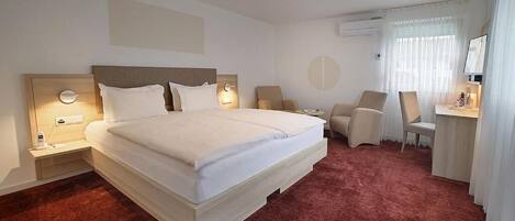 A hotel room with a large bed, two bedside tables with lamps, a desk with a chair, and a large window with curtains.