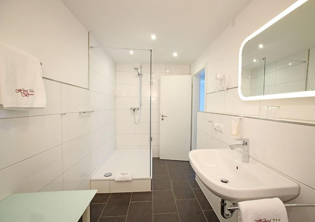 A modern bathroom with a glass-enclosed shower, a white sink, and a large mirror.
