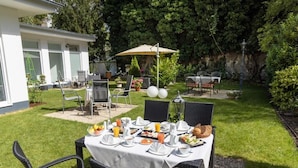 An outdoor dining area with a table set for breakfast, surrounded by chairs and an umbrella.