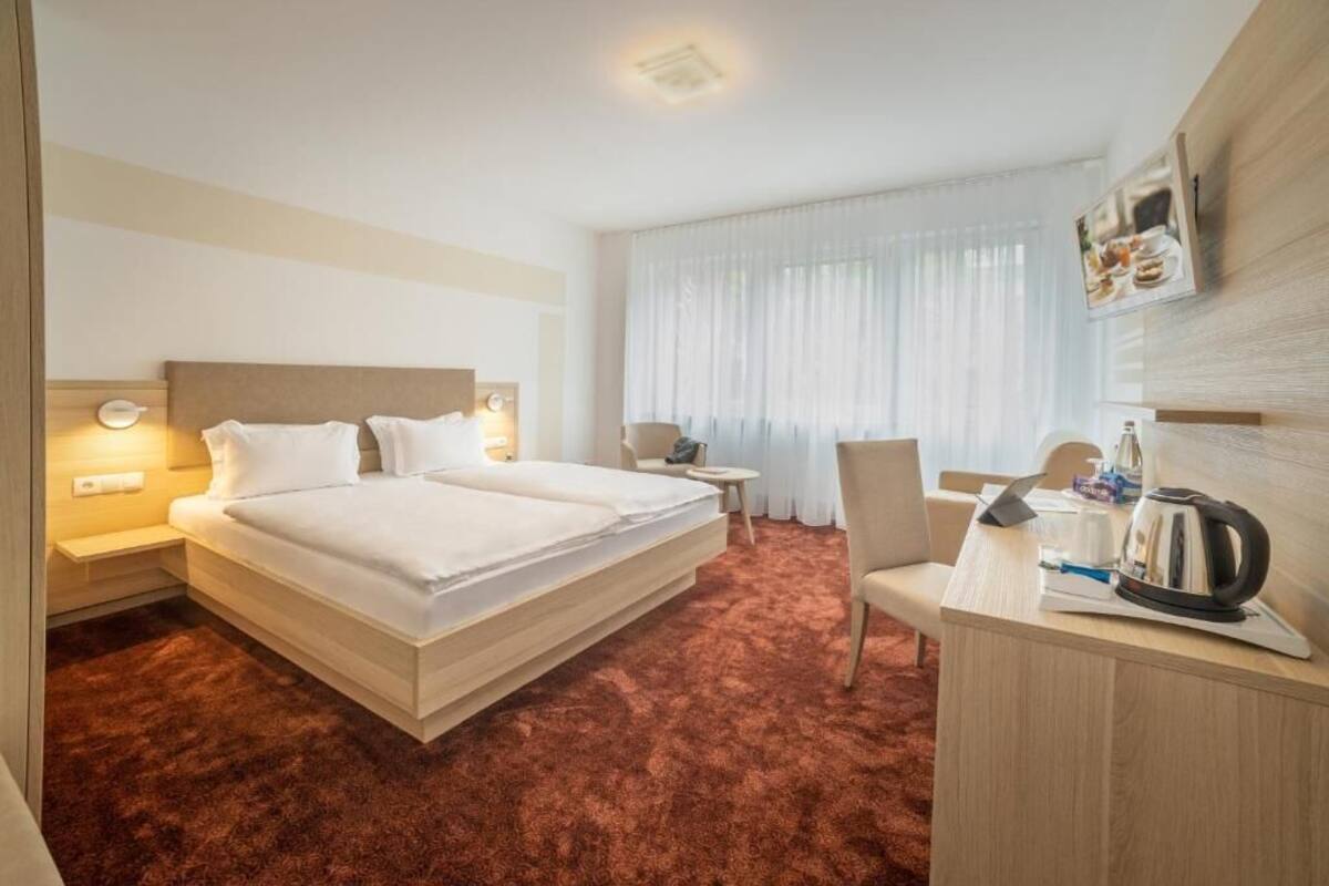 A hotel room with a large bed, a desk, a chair, and a small table.