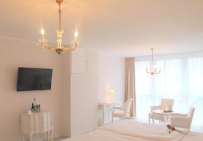 A hotel room with a large bed, a desk with a chair, a TV mounted on the wall, and a chandelier. - Hotel Brenner (Koblenz)