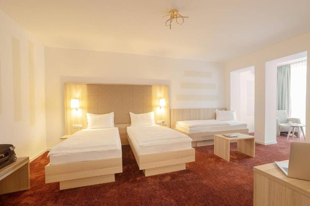 A hotel room with two beds, a desk, a chair, and a small table.