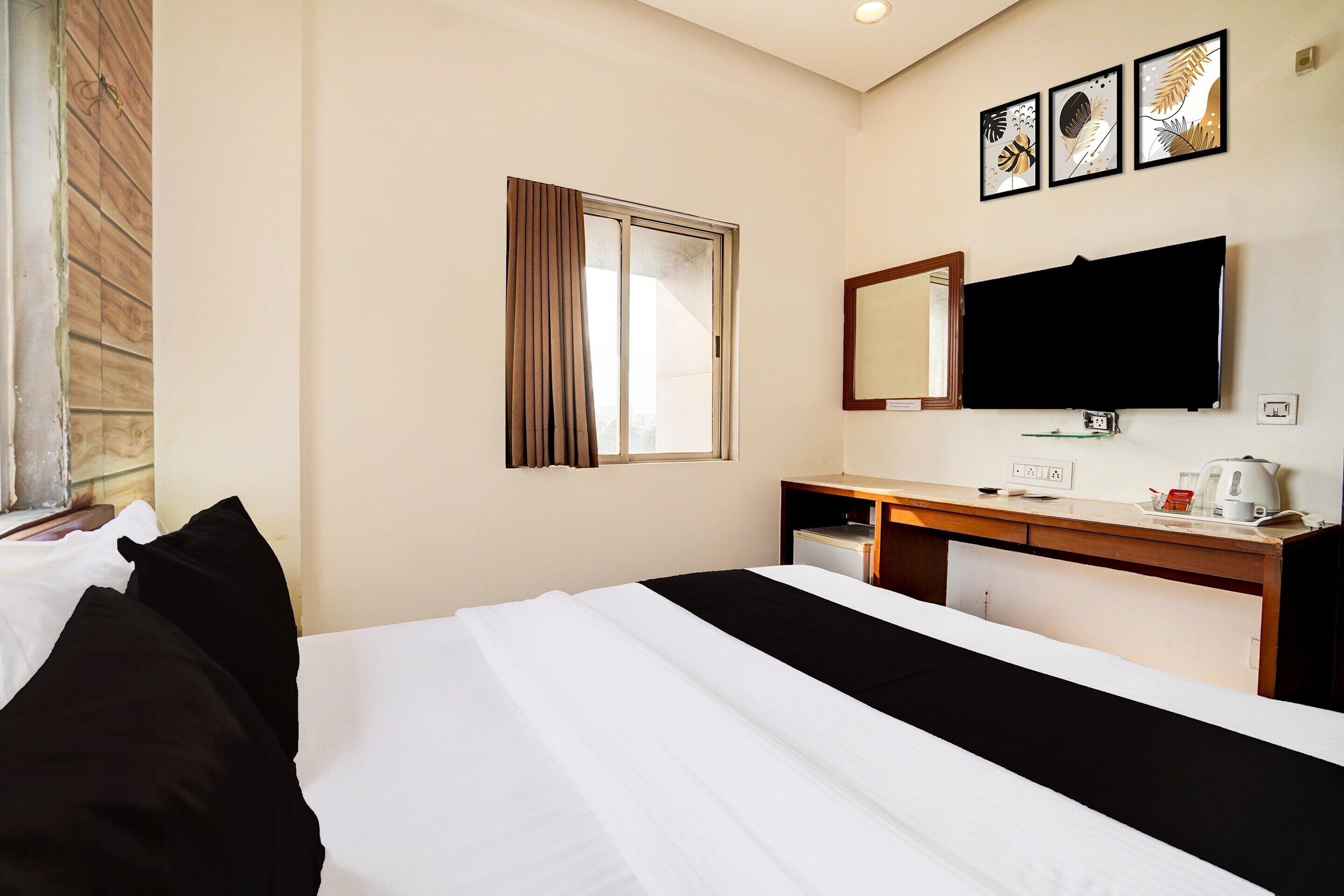 Habitación de hotel con cama, escritorio, televisor de pantalla plana, espejo y ventana con cortinas.