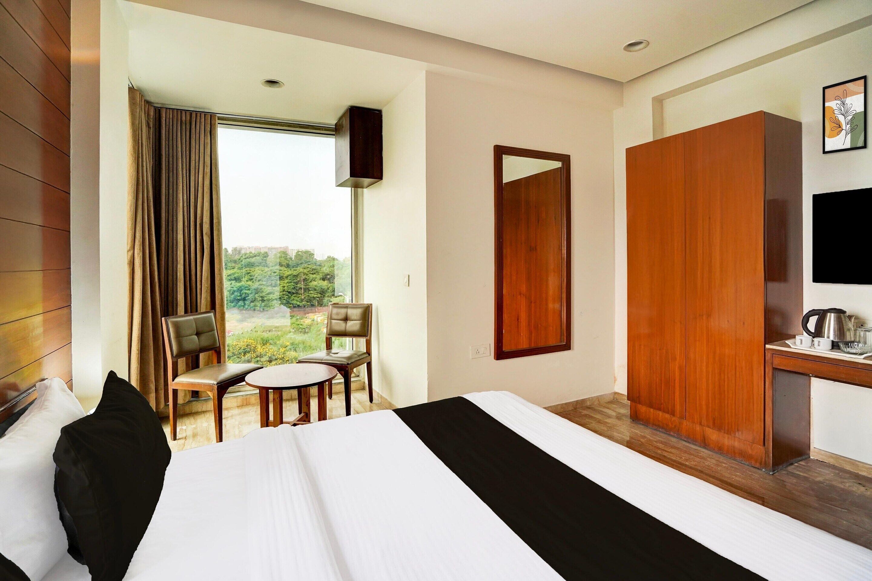 Habitación de hotel con cama, escritorio con silla, ventana con cortinas y vista a zonas verdes.