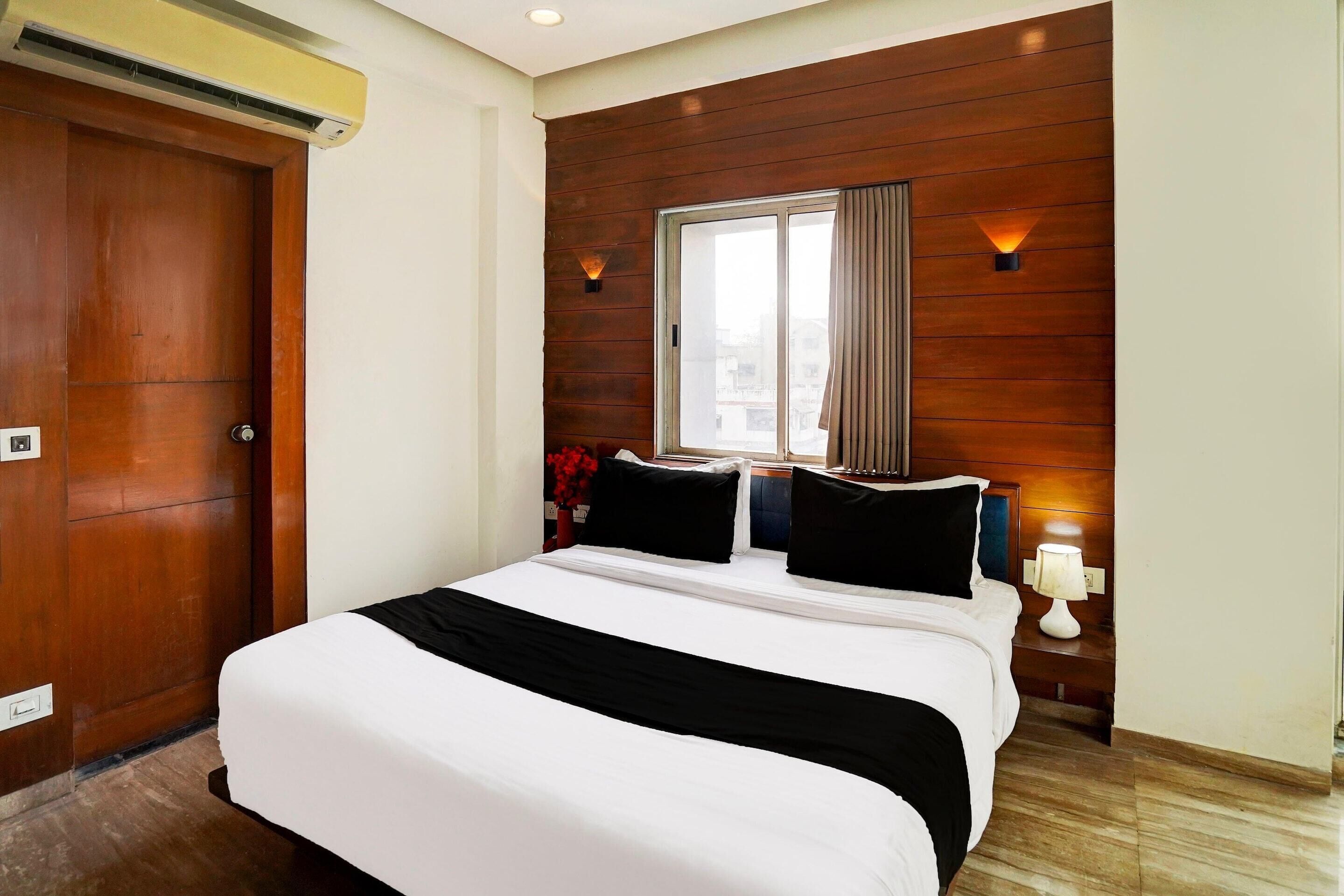 A hotel room with a large bed, wooden panel walls, a window with curtains, and a nightstand with a lamp.