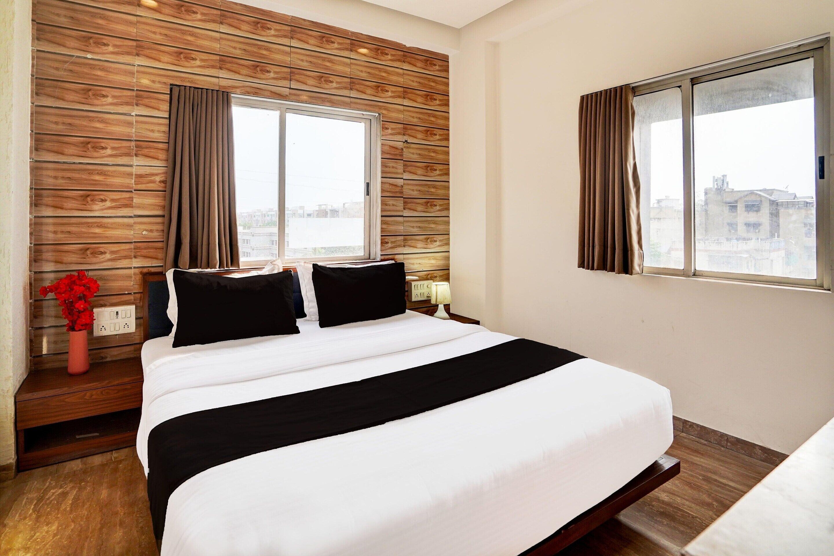 Camera d'albergo con parete rivestita in legno, un letto grande con biancheria in bianco e nero, due comodini con lampade e una finestra con tende.