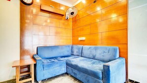 A corner room with a blue sofa, a small wooden table, a wall-mounted fan, and a clock. - Super Collection O Airport Road Hotel (Ahmedabad)