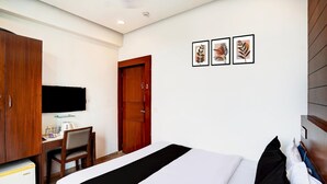 A hotel room with a bed, a desk with a chair, a wardrobe, and a television. - Super Collection O Airport Road Hotel (Ahmedabad)
