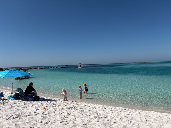Una playa con aguas turquesas cristalinas, un barco a lo lejos y gente disfrutando de la orilla.
