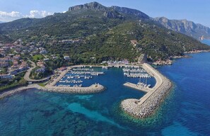 An aerial view of a coastal town with a marina, clear blue waters, and a mountainous backdrop. - Large cozy house 400 meters from the sea ideal for families and groups (Santa Maria Navarrese)