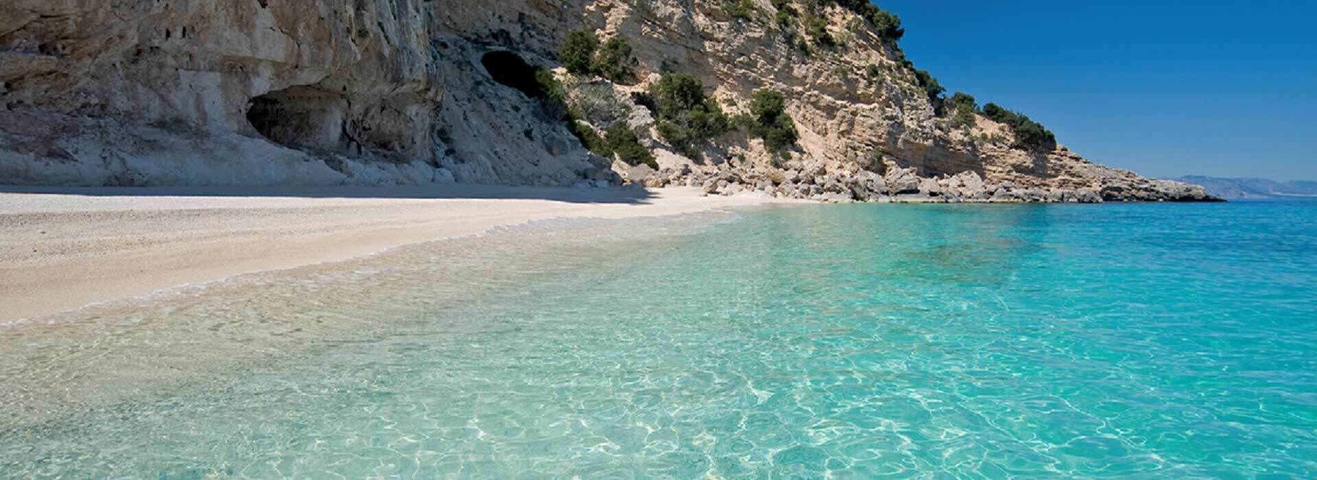 Uma praia com águas turquesa cristalinas, areia branca e falésias rochosas.