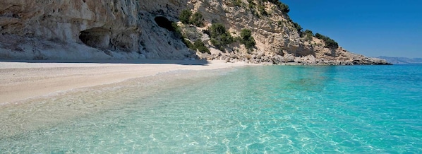 Uma praia com águas turquesa cristalinas, areia branca e falésias rochosas.